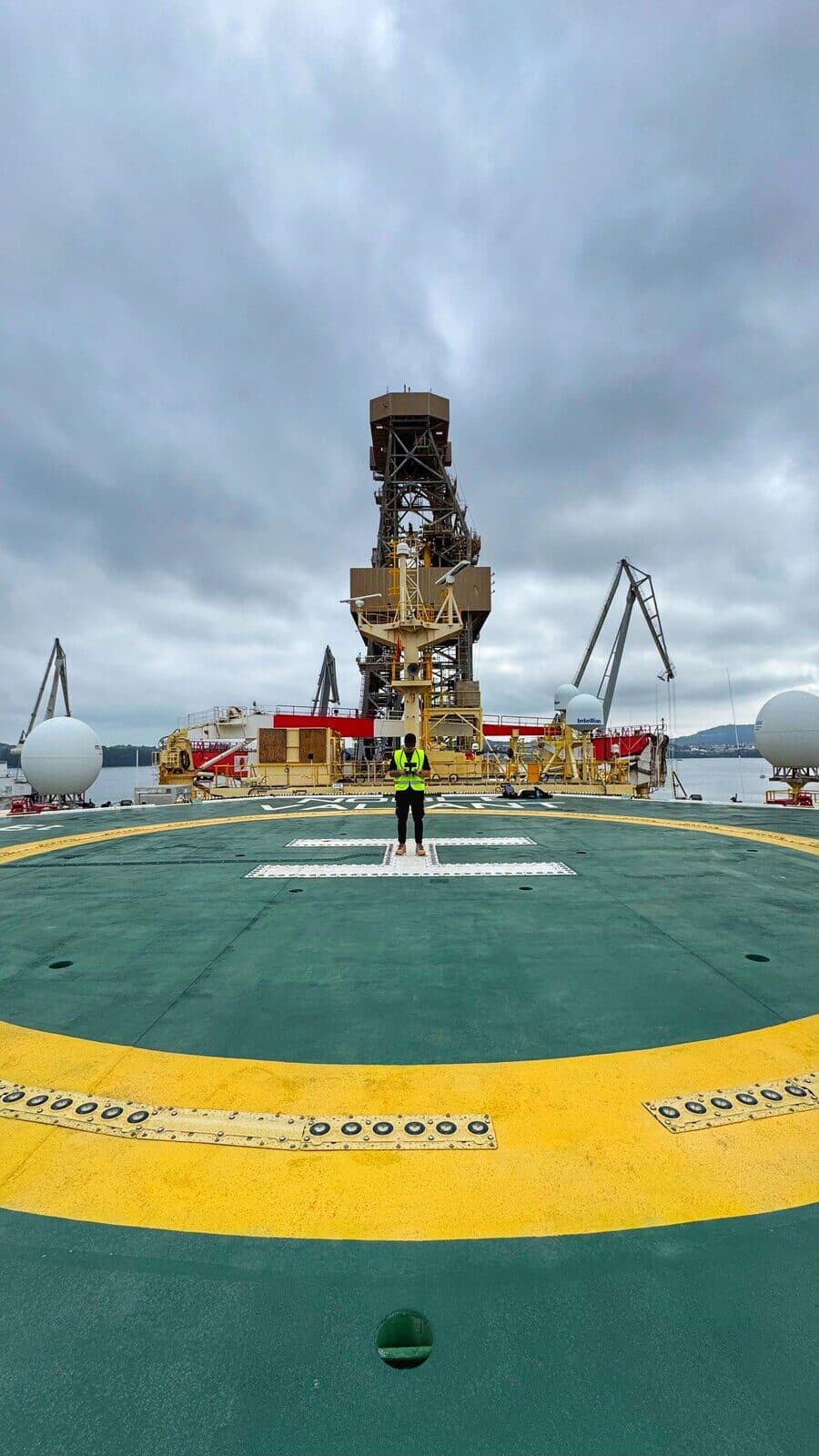 Persona de pie en el helipuerto de una plataforma industrial marina, mostrando la escala real captada desde el aire