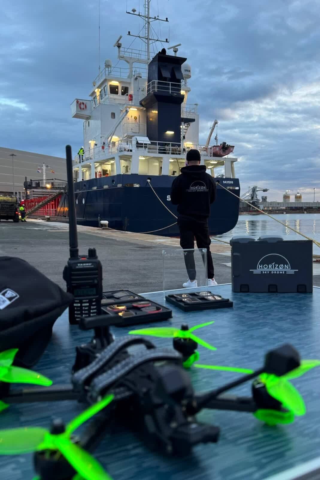 Piloto de Horizon Sky Drone preparando un vuelo FPV junto a un buque en un puerto, al atardecer