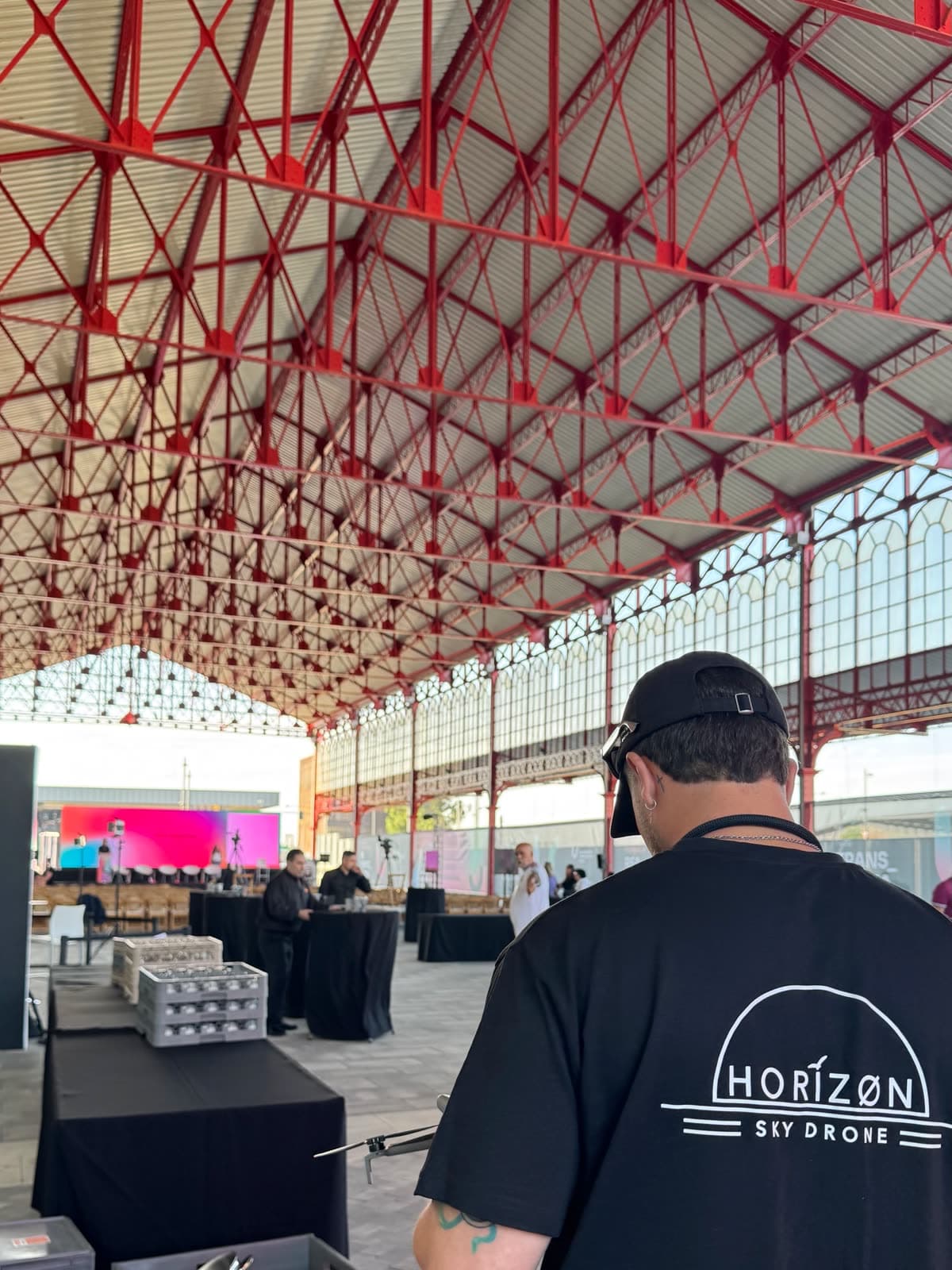Piloto de Horizon Sky Drone con dron en mano, con camiseta de la marca, durante un evento corporativo en una nave industrial